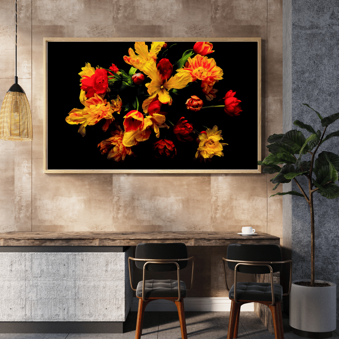 Een modern interieur met een grote ingelijste foto van levendige rode en gele bloemen tegen een zwarte achtergrond. Onder de foto staat een houten tafel met twee zwarte stoelen. Links hangt een rieten lamp en rechts staat een kamerplant in een witte pot. De ruimte heeft beige textuurdmuren en een grijs stenen bargedeelte.