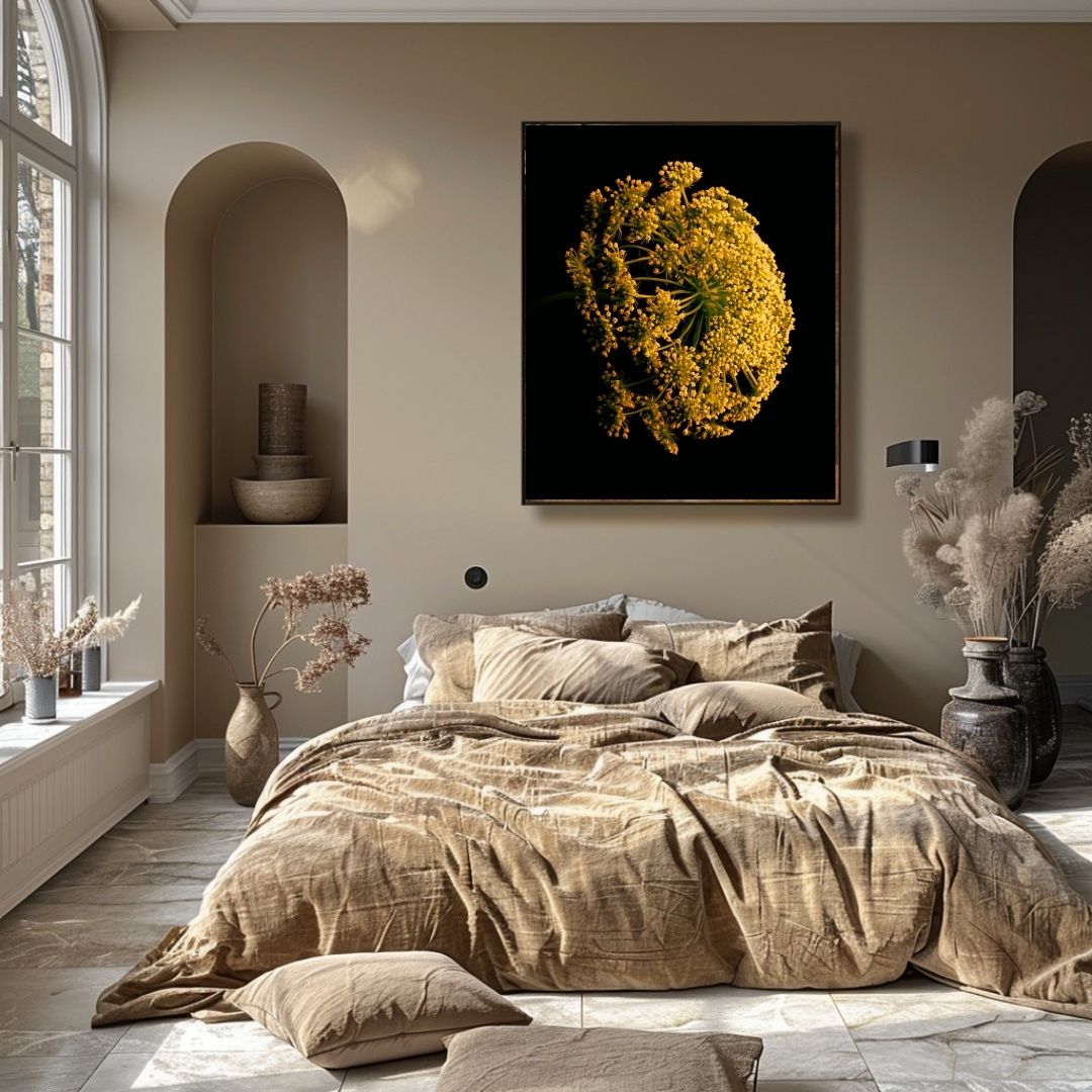 Slaapkamer in naturel tinten met beige muren en bedtextiel. Boven het bed hangt een zwart ingelijst kunstwerk van een goudgele zevenblad bloem. Links grote ramen met boogvormige nis waarin keramiek staat. Decoratieve droogbloemen in vazen aan beide zijden van de kamer. Rustgevende, minimalistische sfeer.