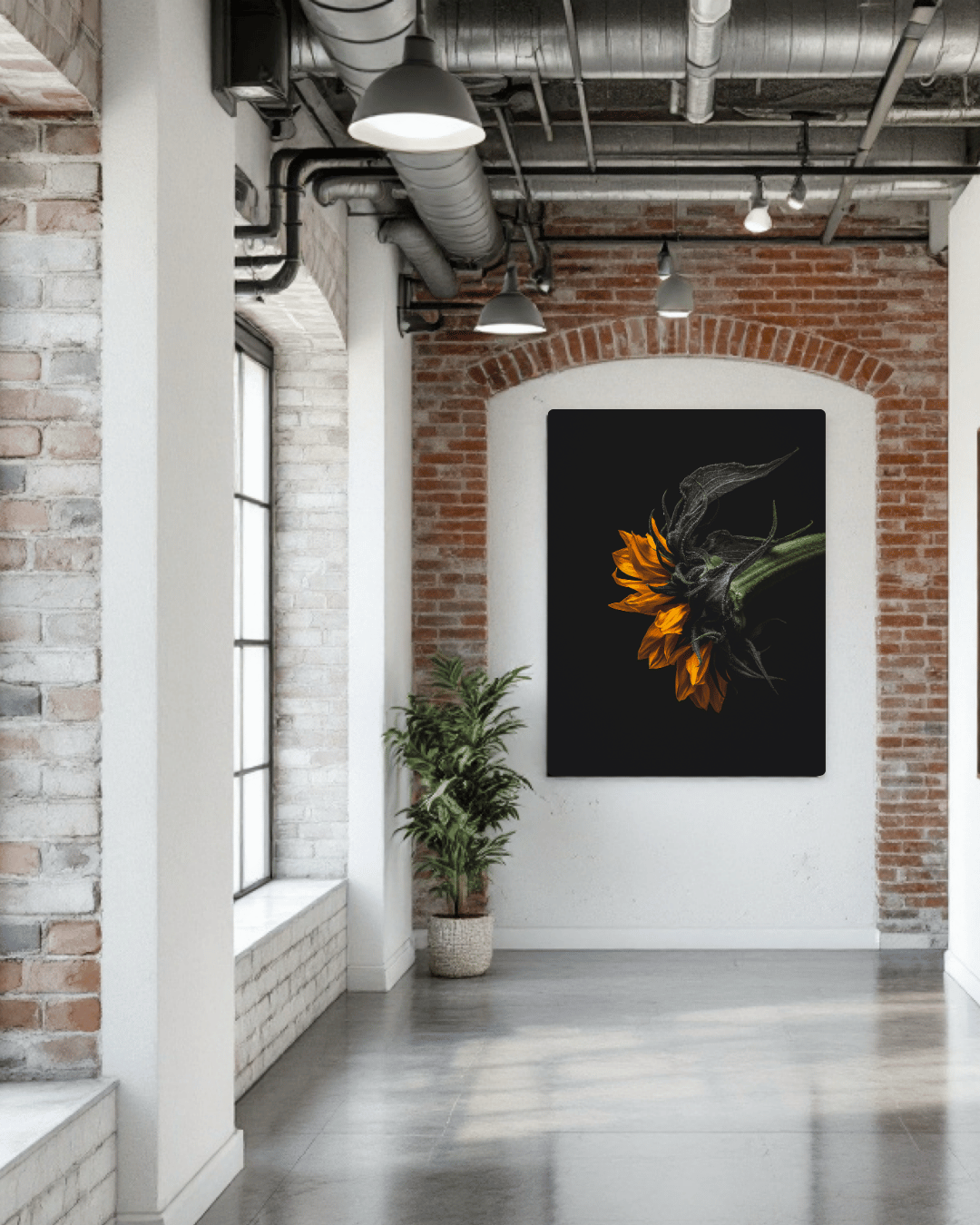 De afbeelding toont een industriële, loft-achtige ruimte met bakstenen muren in rood en wit. In het midden van de ruimte hangt een stijlvol kunstwerk met een oranje/gele zonnebloem tegen een zwarte achtergrond. Dit kunstwerk contrasteert mooi met de ruwe bakstenen muur erachter en is geplaatst in een witte nis met een bakstenen boog erboven.